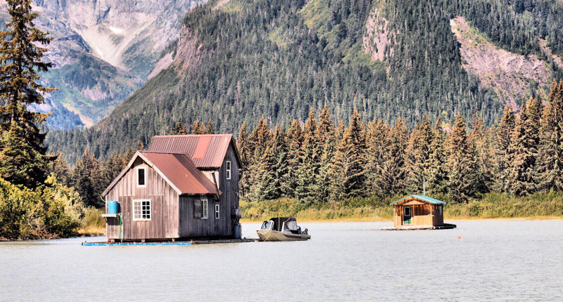 OLYMPUS DIGITAL CAMERA a small house in a body of water with a mountain in the background